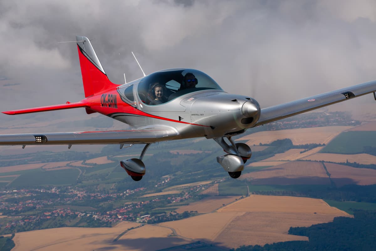 Bristell B23 with two on board over summer countryside