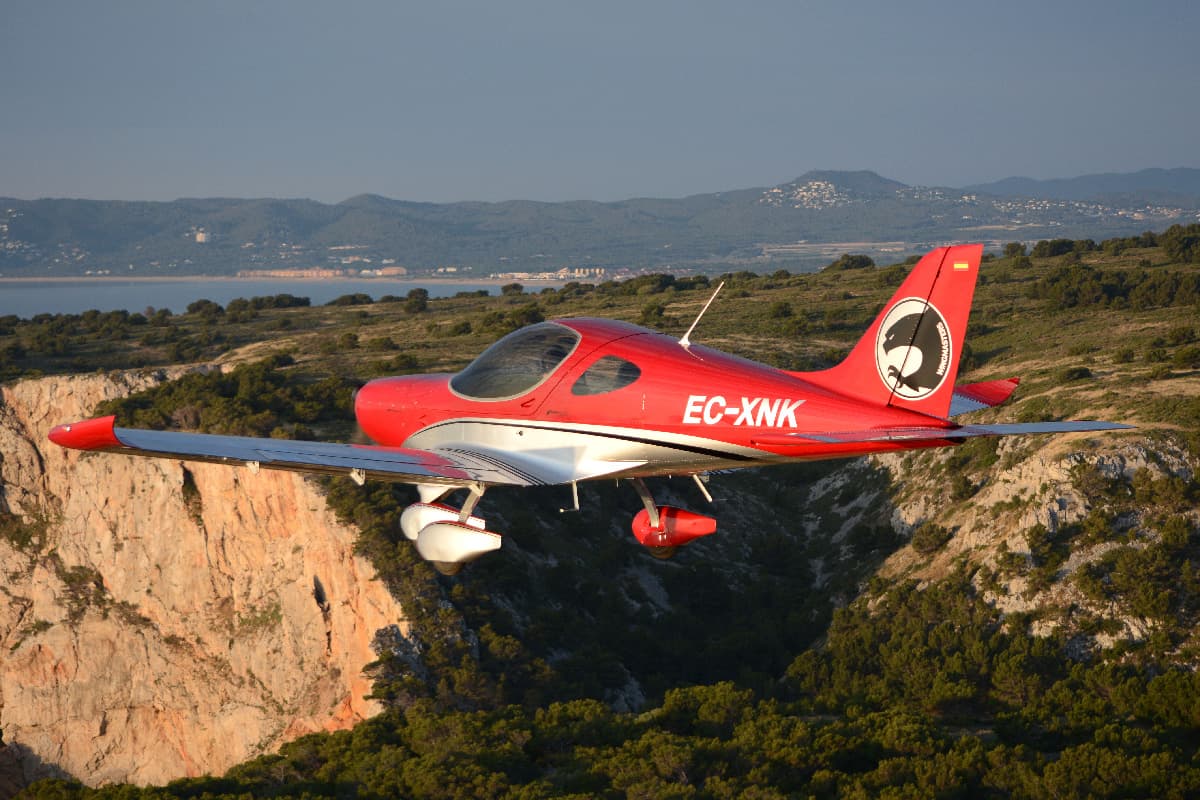 Red Bristell Classic in flight along the coastline