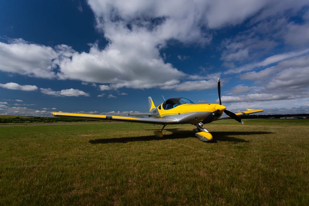 Yellow Bristell Classic on a grass airfield under dramatic clouds